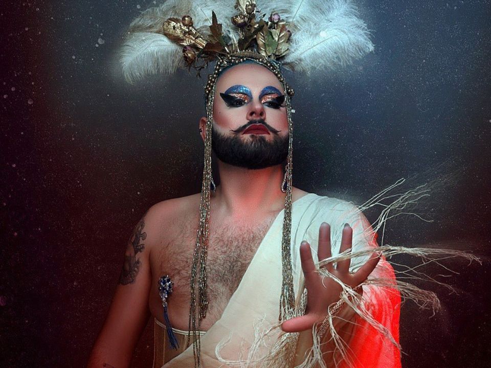 Drag-Queen mit Bart, Feberkrone und goldenem Schmuck